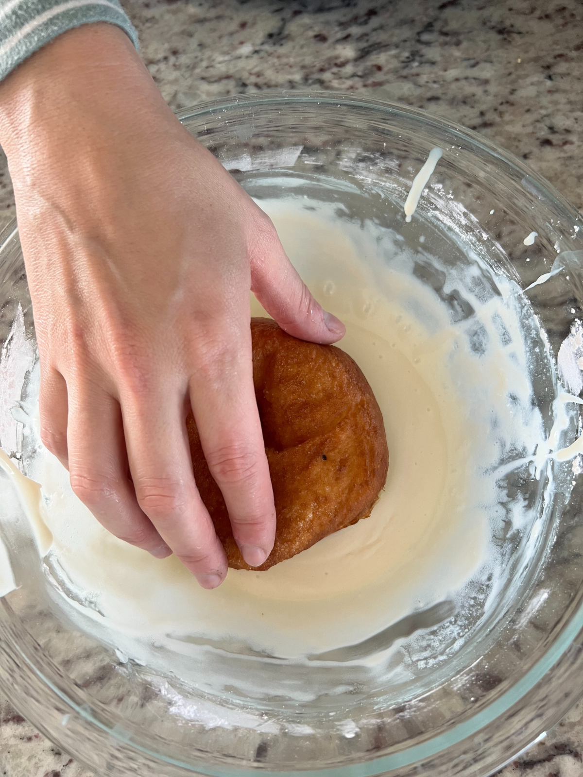 A hand is shown dipping the donuts into the glaze.