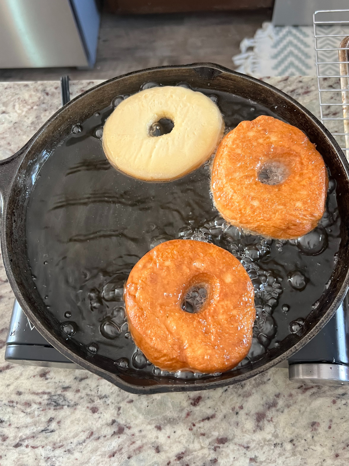 The donuts are shown flipped and cooked on one side in the cast iron skillet.