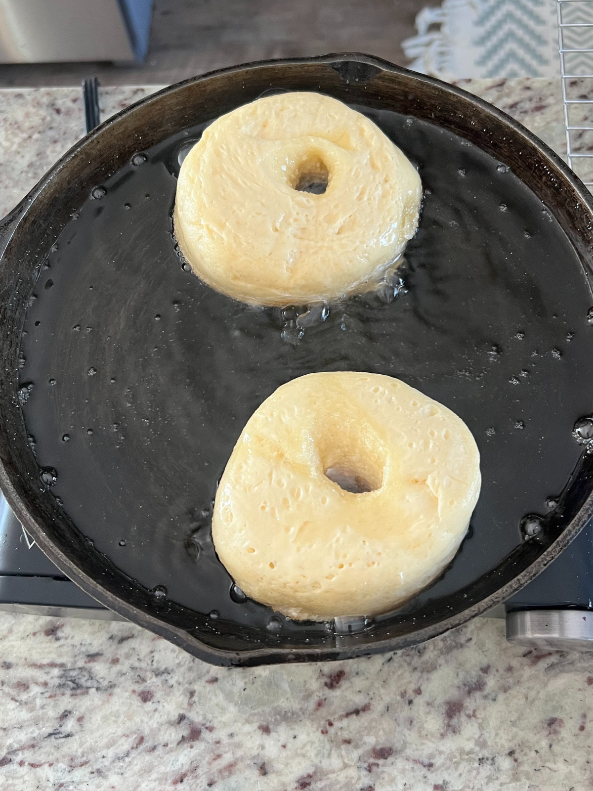 The sourdough donuts are shown frying in coconut oil in a cast iron skillet.