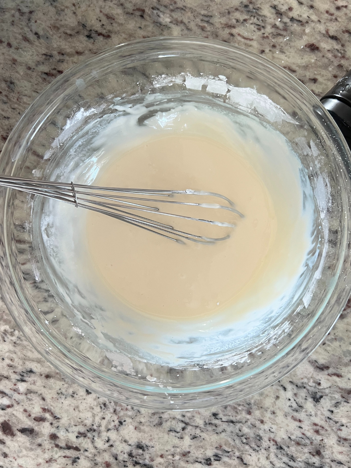 A bowl of homemade glaze for the donuts sits in a glass mixing bowl.