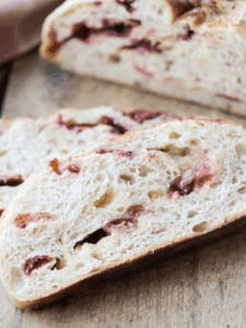 Two slices of sourdough white chocolate strawberry bread sit on a wooden cutting board with half of the loaf in the background.
