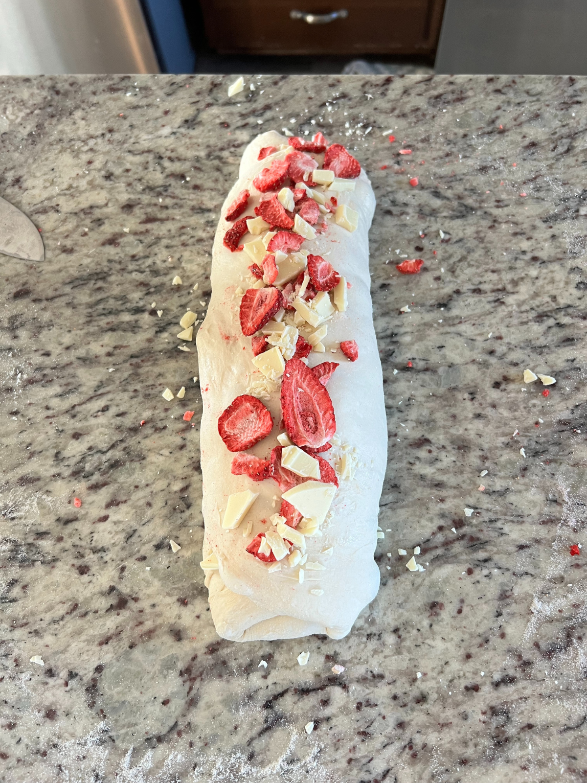 The strawberry white chocolate sourdough dough has been rolled into a cylinder shape and topped with more inclusions.