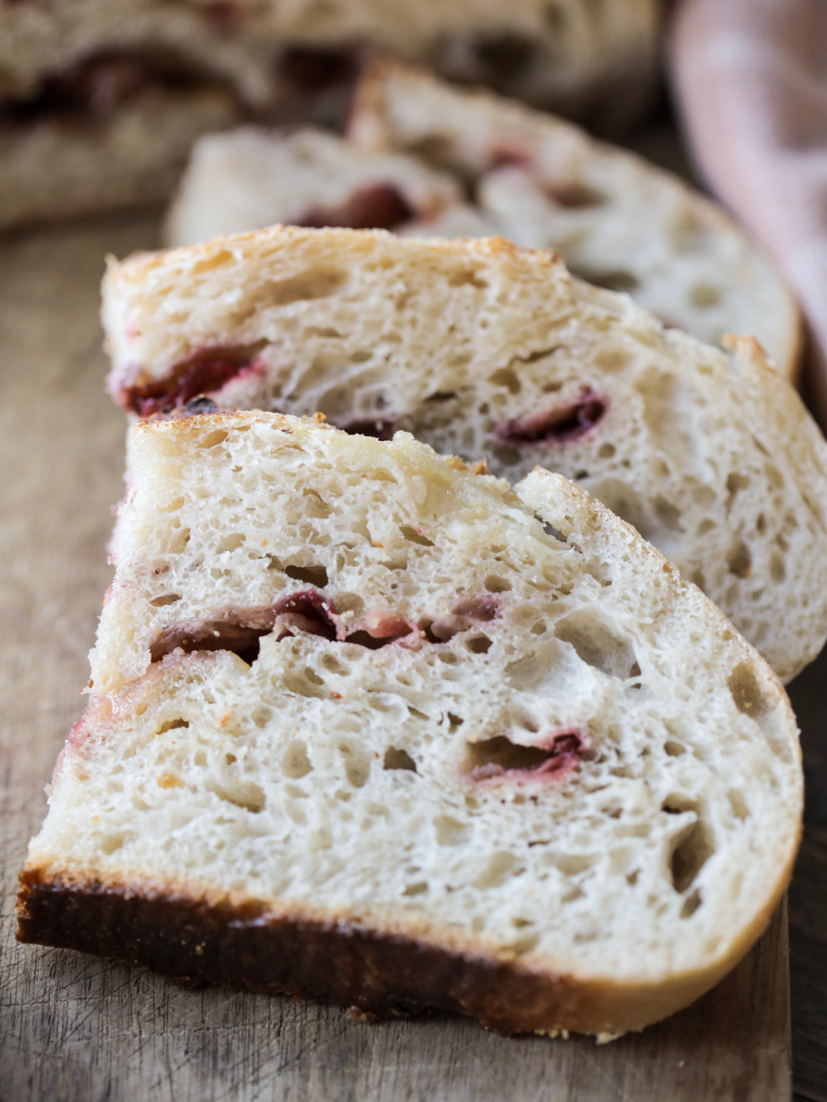 Three half slices of strawberry white chocolate sourdough bread lay on a wooden cutting board.