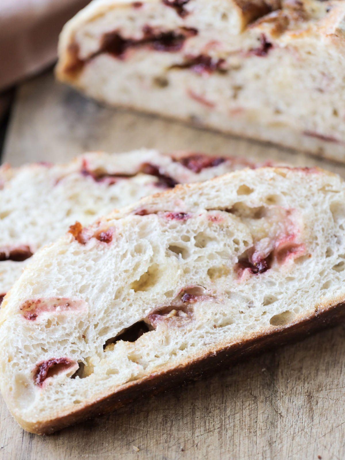 Two slices of sourdough white chocolate strawberry bread sit on a wooden cutting board with half of the loaf in the background.