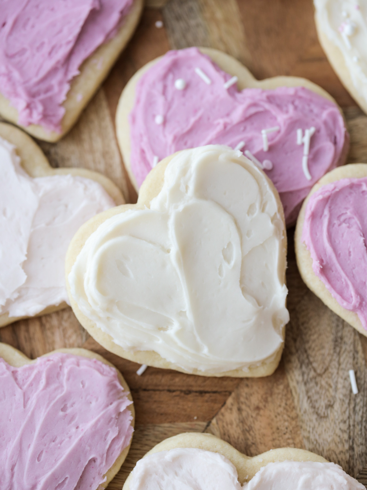 Several heart shaped sourdough discard sugar cookies with buttercream frosting sit on a platter. One cookie is close up and focused.