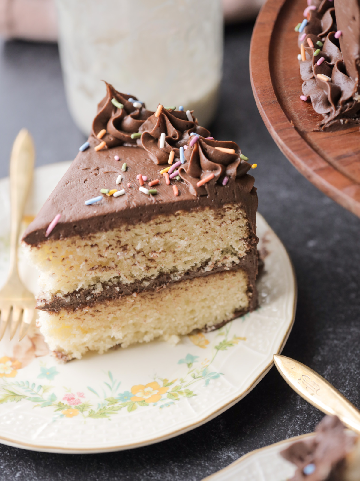 One slice of a two-layered sourdough vanilla birthday cake with chocolate frosting and sprinkles sits on a plate with a fork.