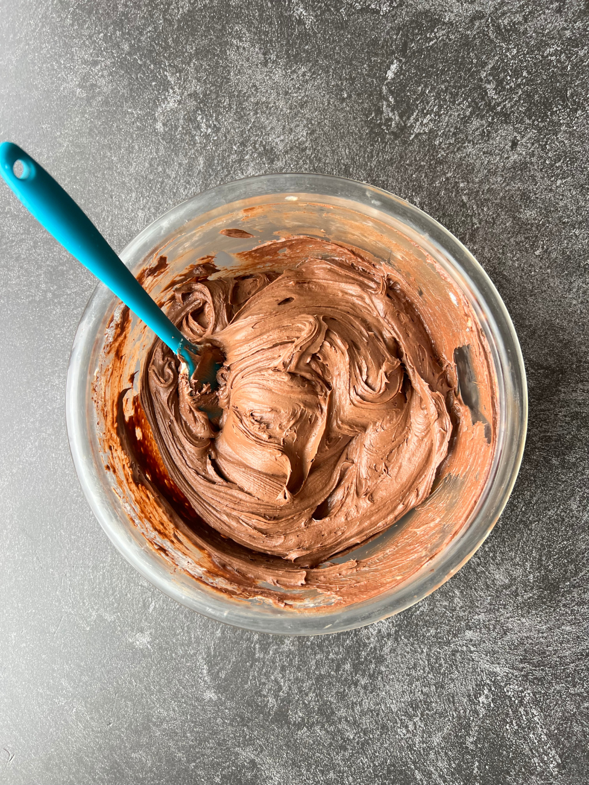 A glass mixing bowl sits with the creamy chocolate cream cheese frosting. 