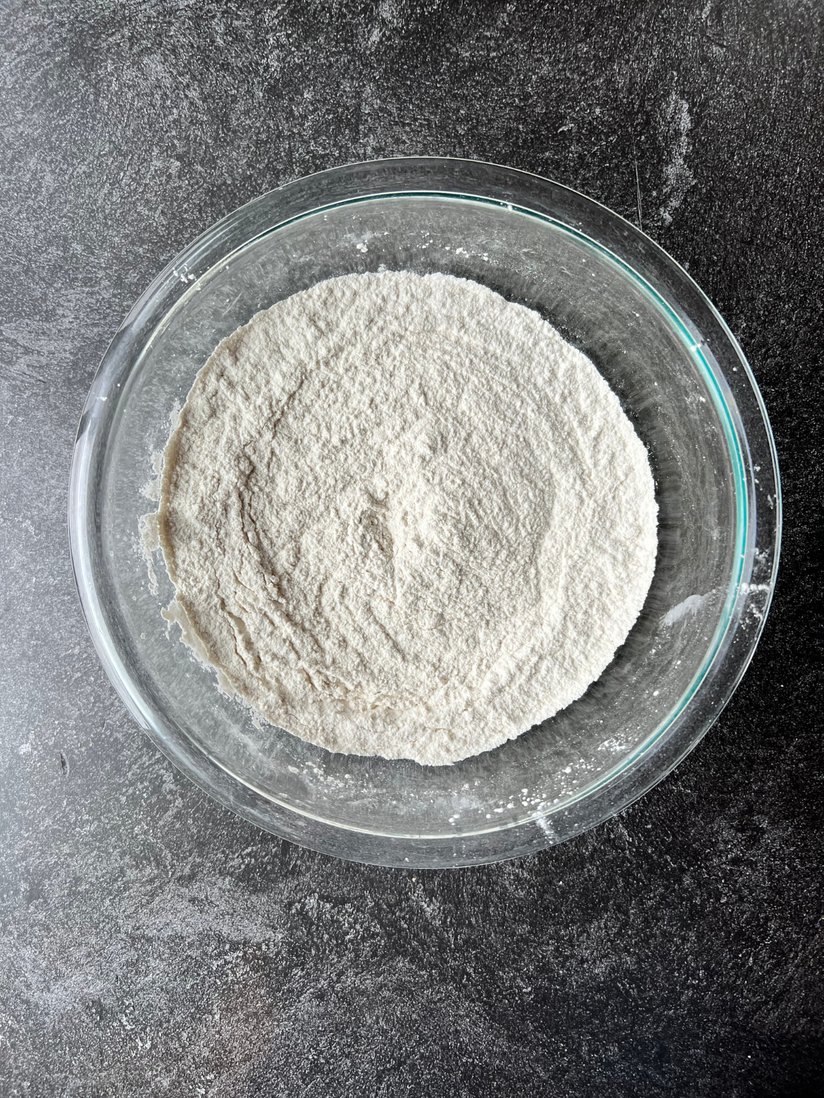 A glass mixing bowl sits with the dry ingredients needed for the sourdough vanilla birthday cake. 