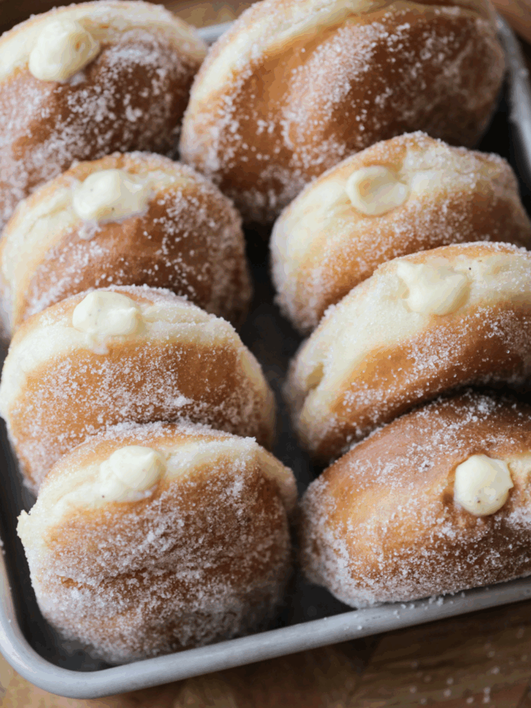 Eight sourdough discard vanilla custard filled donuts sit in a pan.