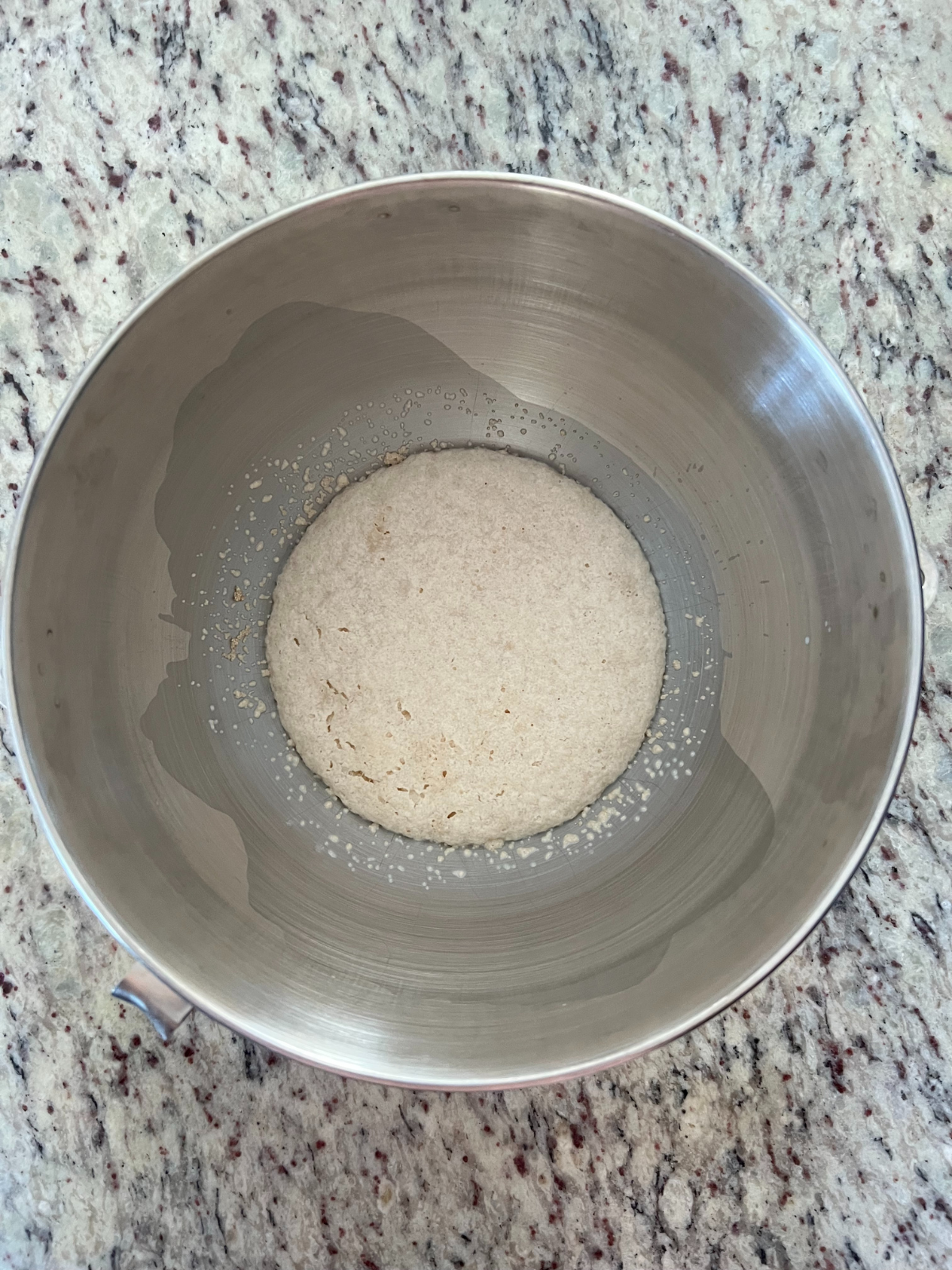 A stand mixer bowl sits with activated yeast, milk, and sugar. 