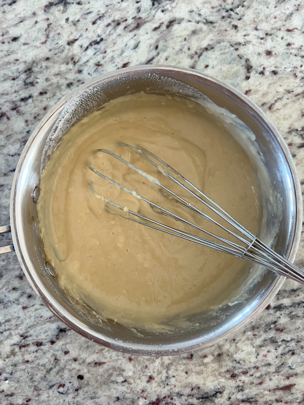 Vanilla custard sits in a medium saucepan with a whisk.