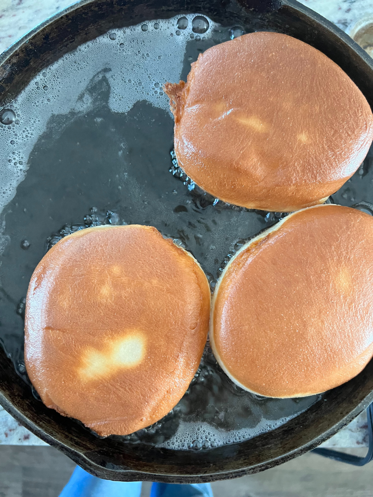Three donuts sit in frying oil browning and cooking on both sides.