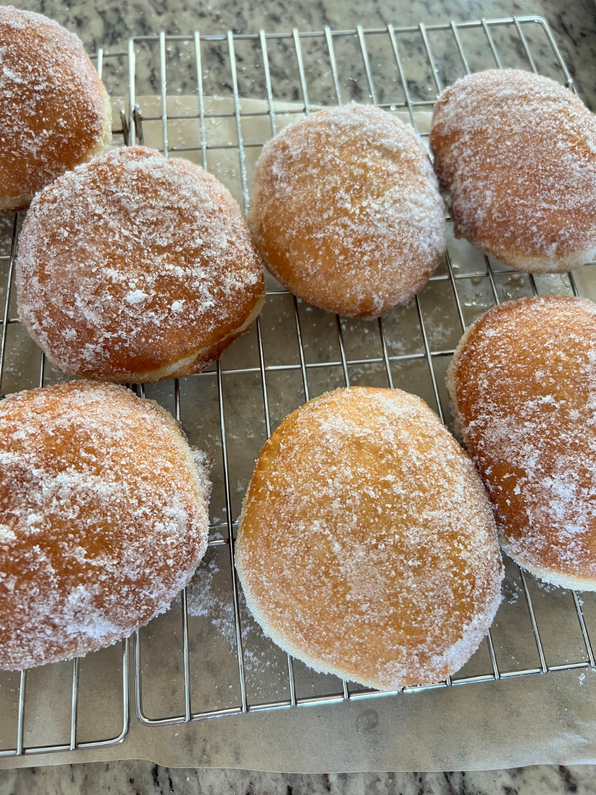 The donuts have been dipped in granulated sugar and sit on a wire rack. Parchment paper sits under the wire rack.