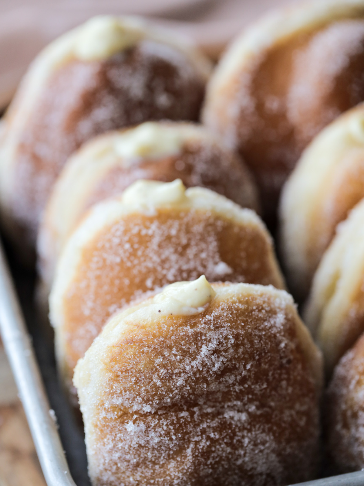 A closeup of one sourdough discard vanilla bean custard donut is shown with several others in the background. 
