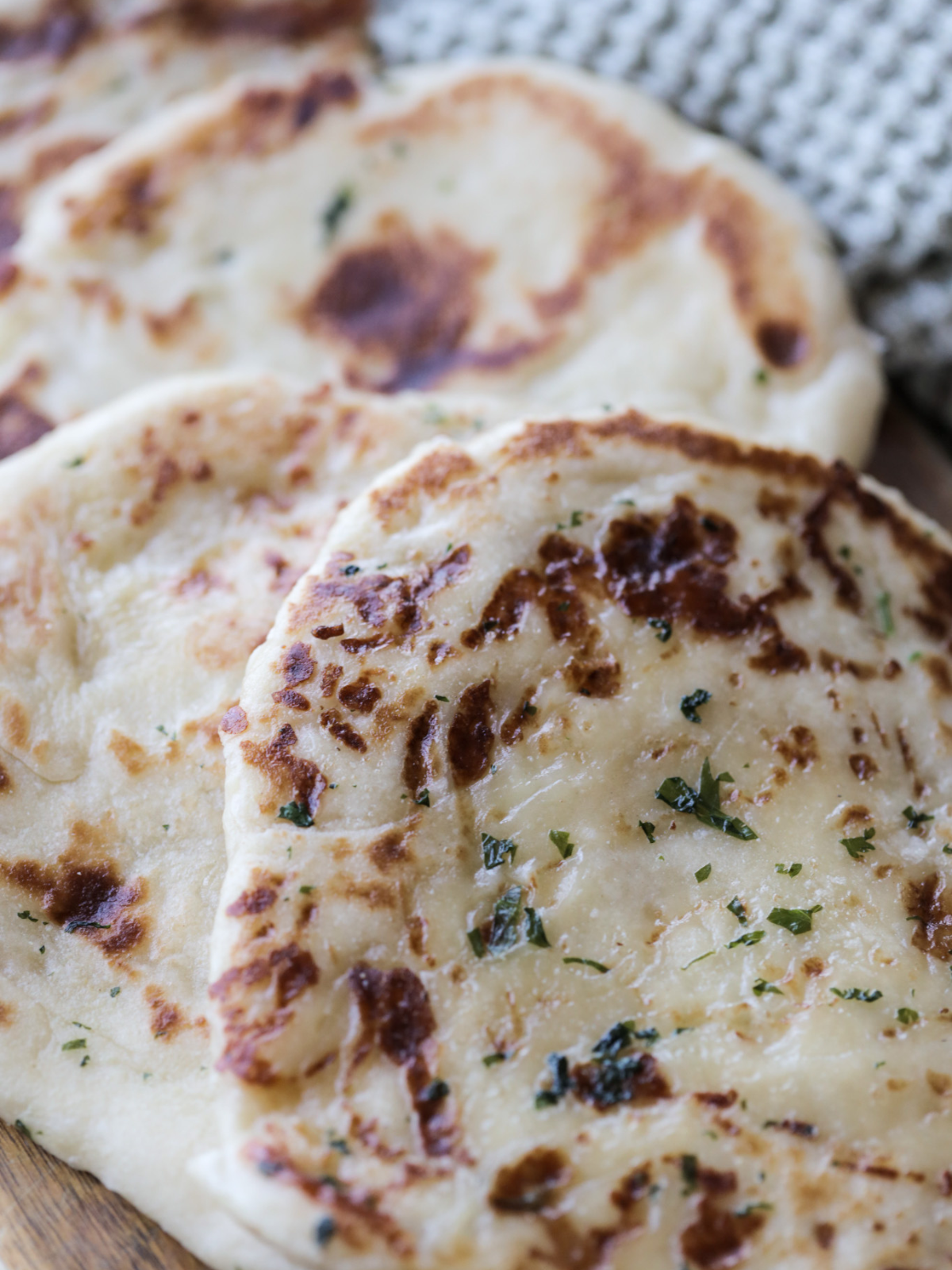 Several sourdough naan sit on a wooden platter. Each sourdough naan is brushed with the herby garlic butter.