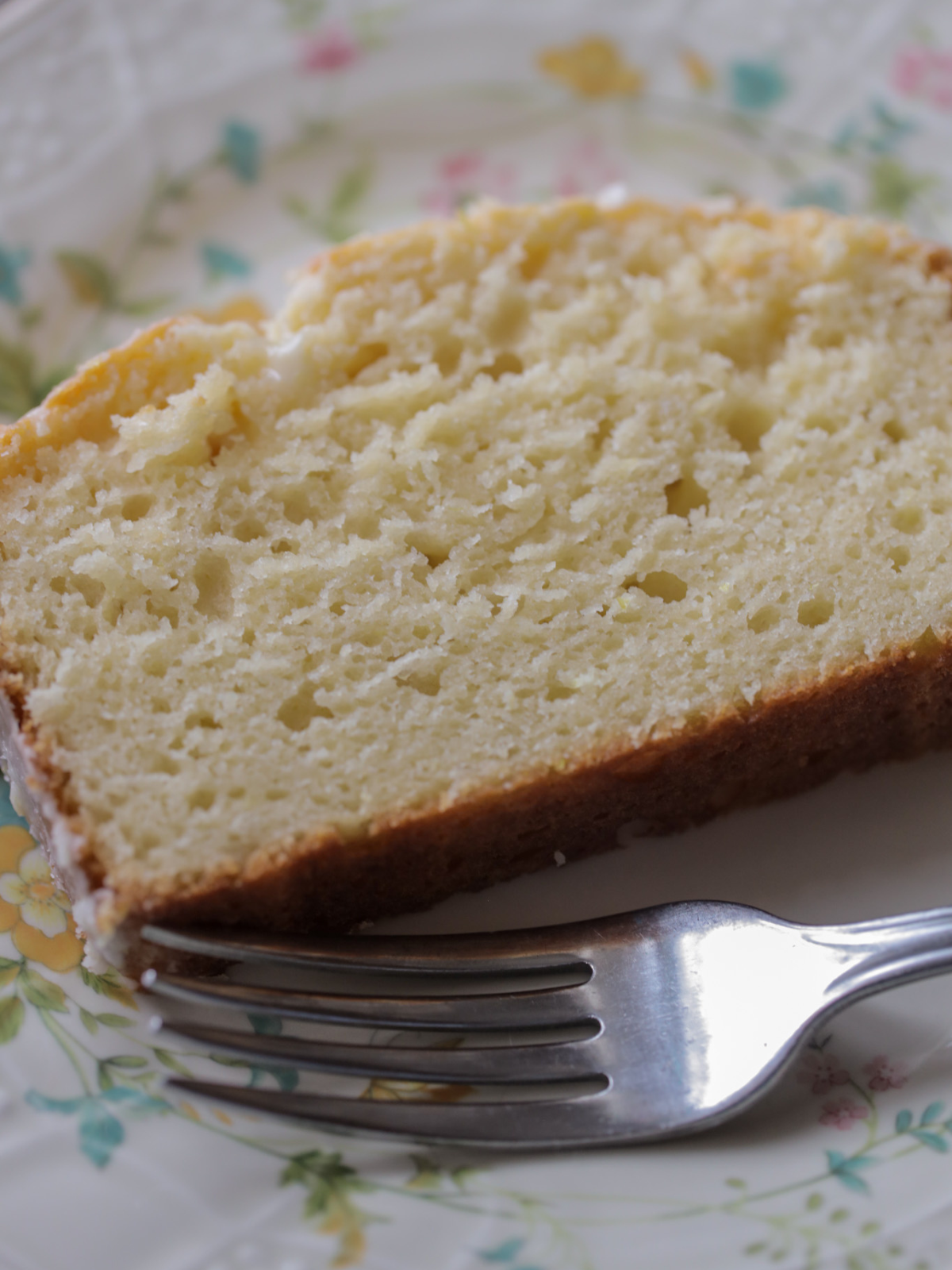 One single slice of sourdough discard lemon pound cake sits on a floral plate. 