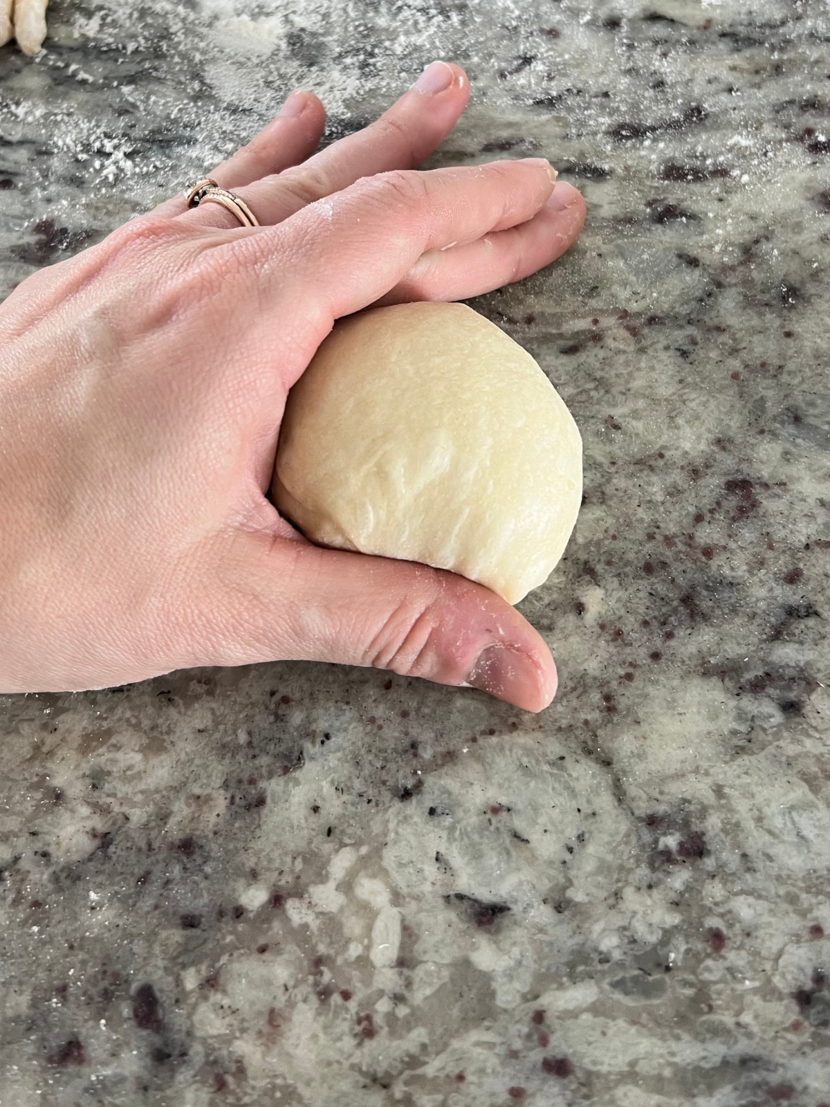 My hand is showing how to roll the brioche sourdough dinner roll dough ball on the counter to shape it into a smooth ball.