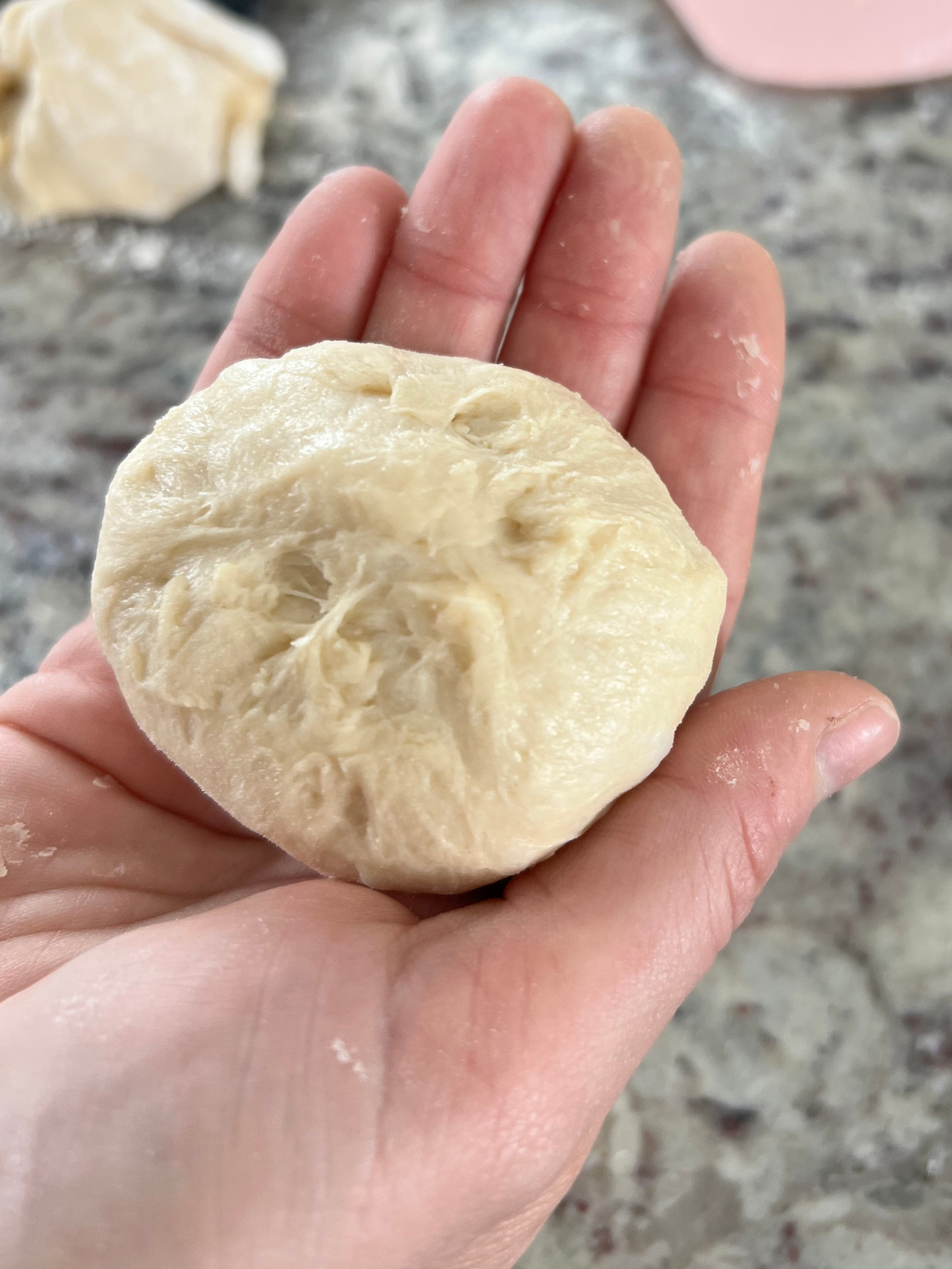 A sourdough brioche dinner roll dough ball sits in my hand after having been pinched in the back.