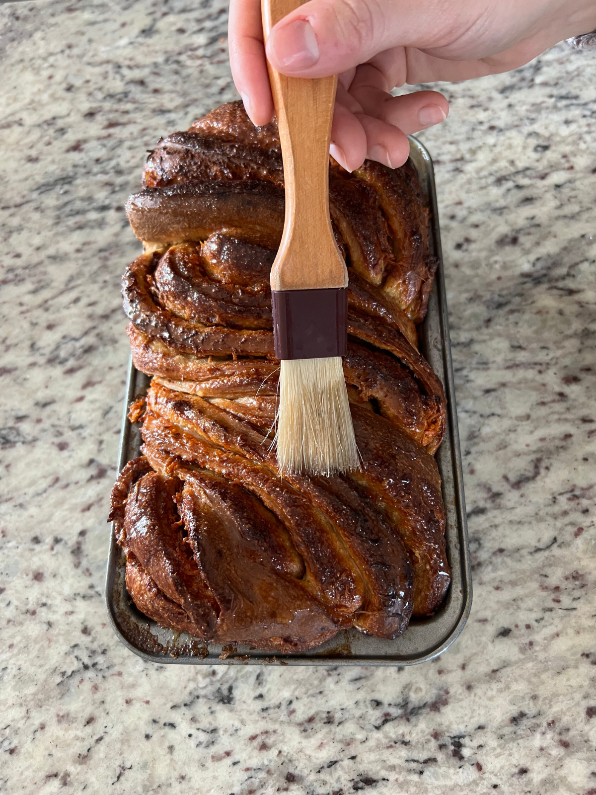 Simple syrup is being brushed over the sourdough carrot cake babka loaf fresh out of the oven.