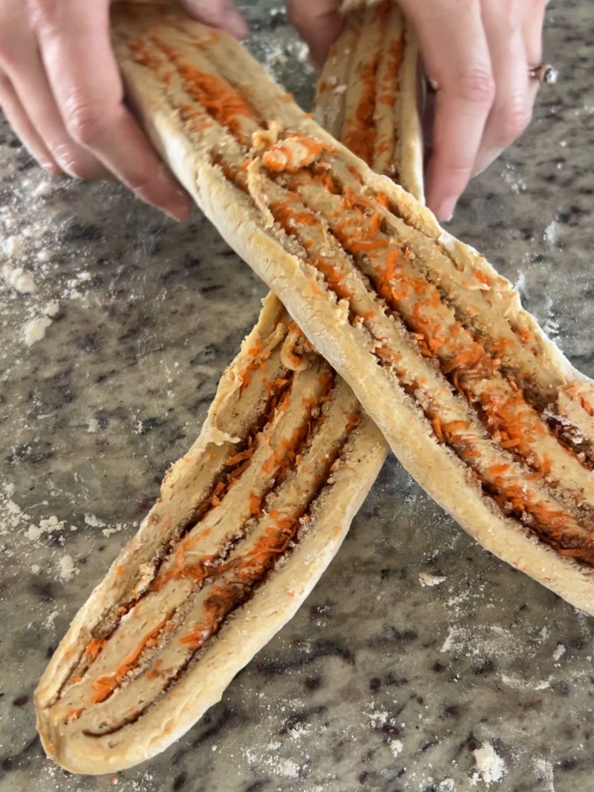 The two strips of carrot cake sourdough babka dough are being braided, first showing one over the other.