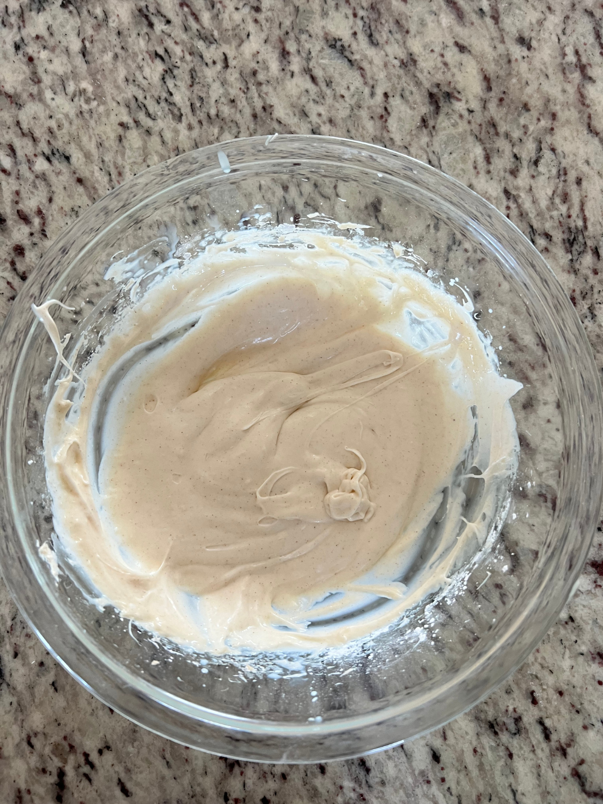 A bowl of cinnamon cream cheese frosting sits in a glass mixing bowl to prepare to spread over the top of the sourdough carrot cake babka.