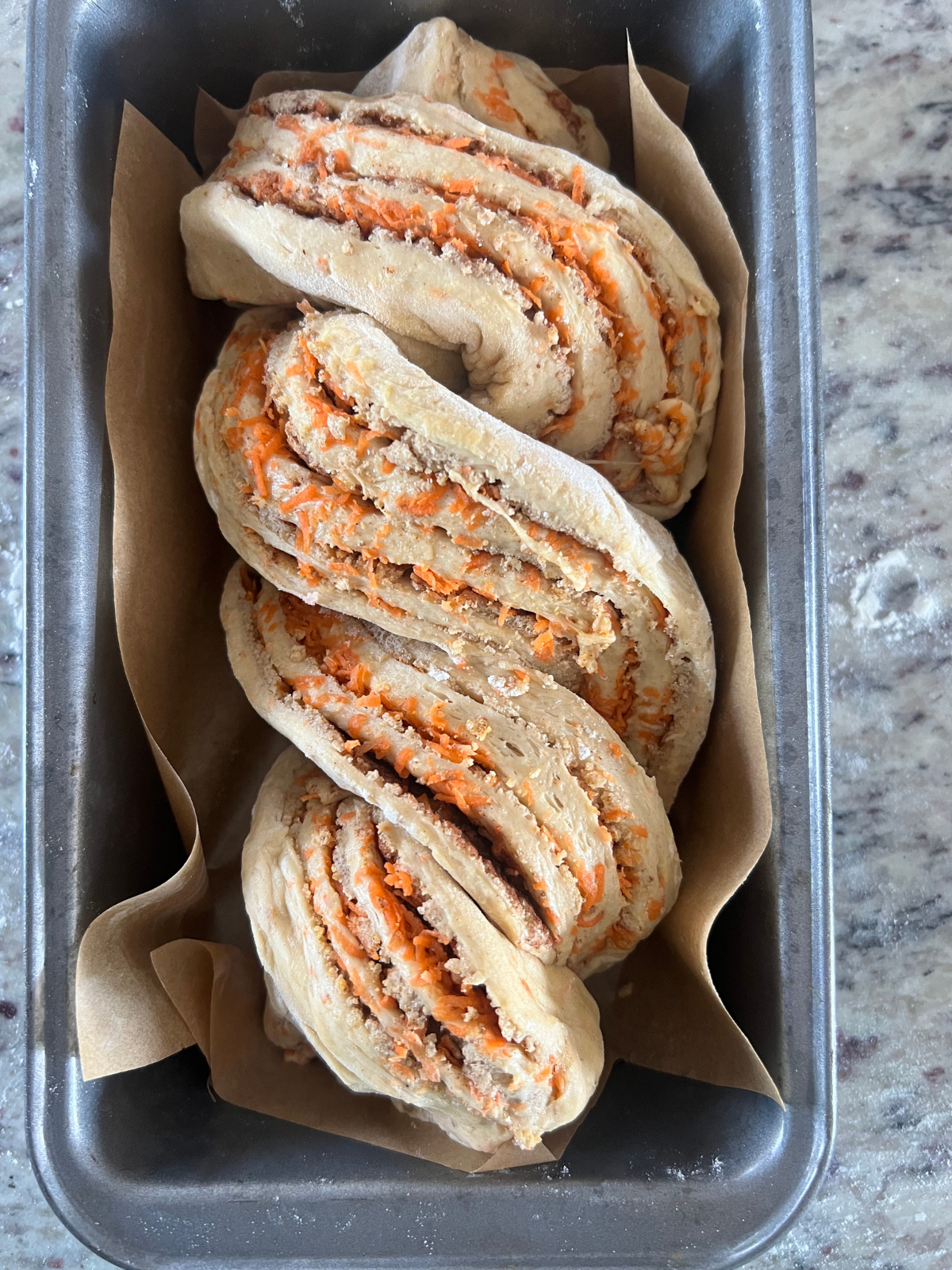 The sourdough carrot cake babka dough sits braided in a parchment paper lined loaf pan.