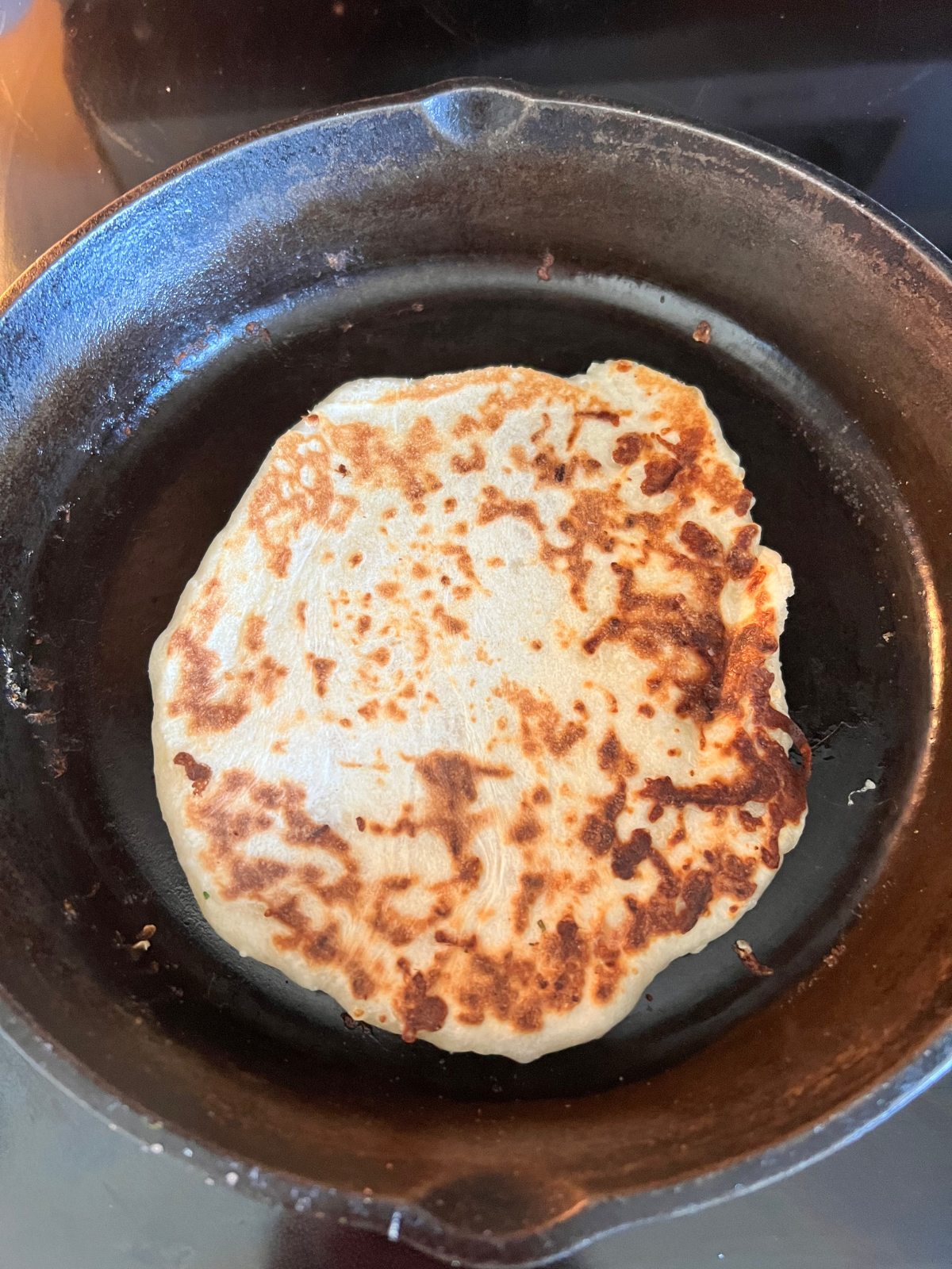 The sourdough naan is shown cooked and sitting on a cast-iron skillet.