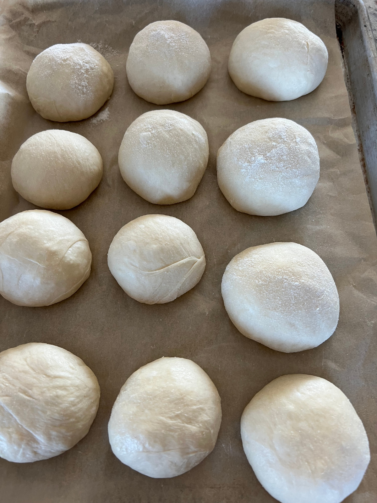 The sourdough mozzarella cheese-stuffed dough balls rest on a parchment paper lined baking sheet where they will rest for about 30 minutes before they will be rolled out and cooked over the stove.