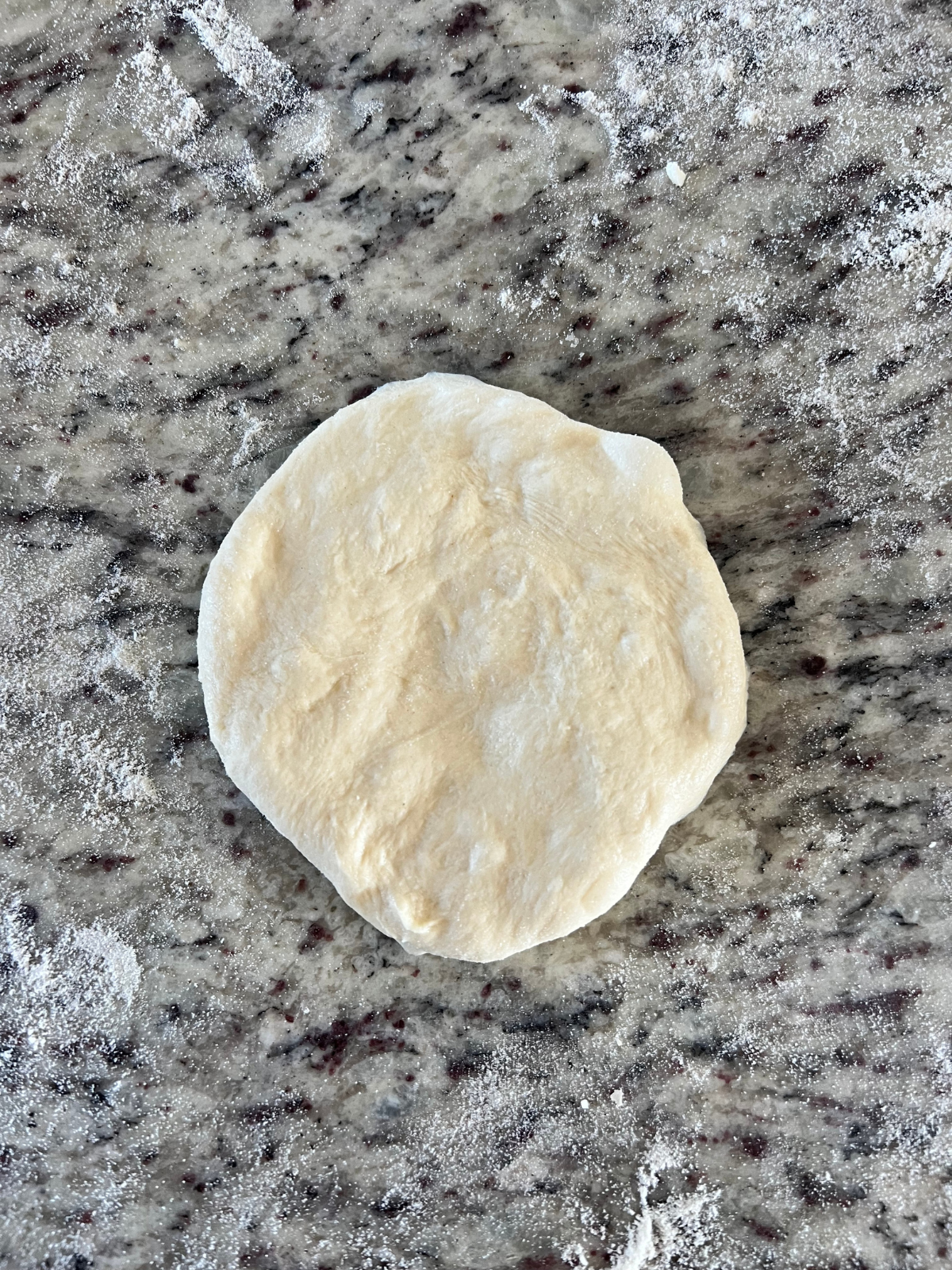 One dough ball sits flattened on the counter ready to have the cheese added. 
