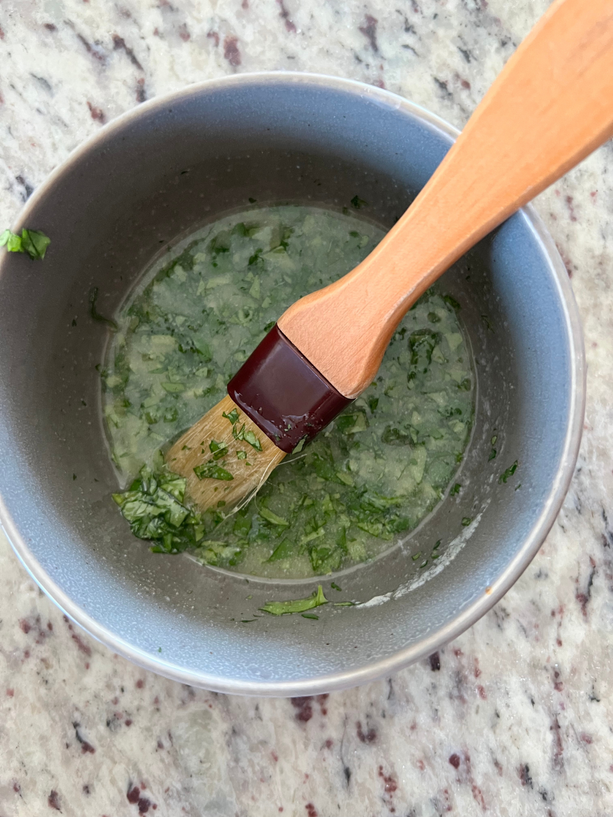 A bowl holds melted butter, garlic salt, and chopped cilantro with a pastry brush that will be brushed over the sourdough naan.