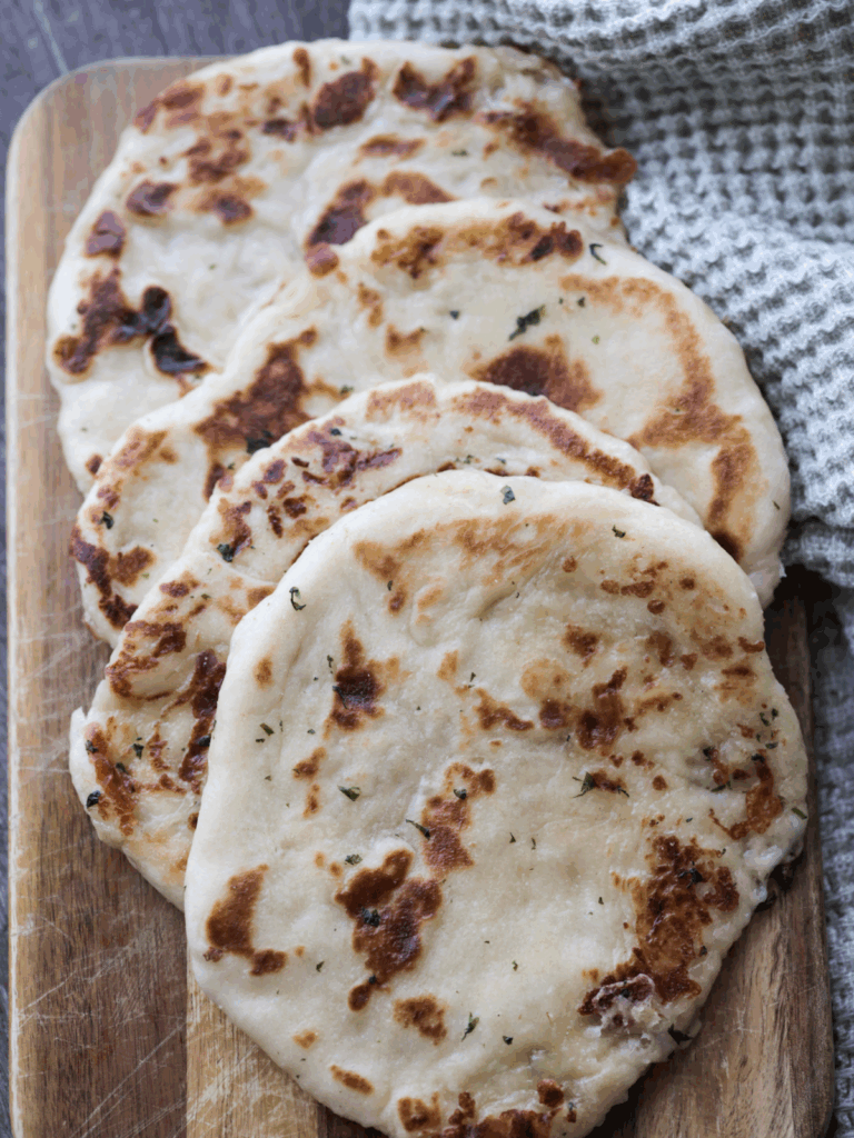 Four mozzarella cheese-stuffed garlic butter sourdough naan sits on a wooden serving board.