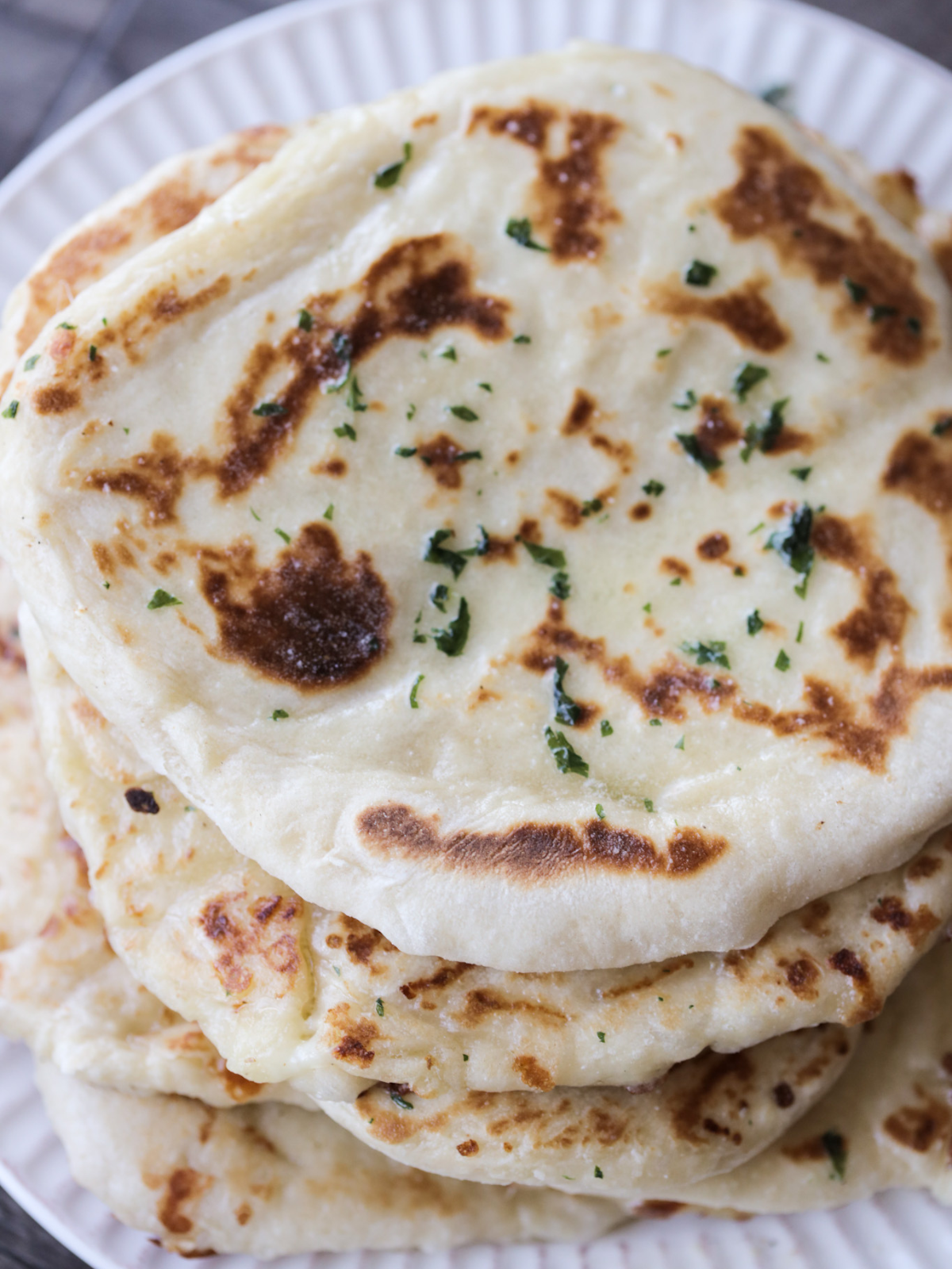 A plate holds a stack of sourdough mozzarella cheese-stuffed naan with garlic butter brushed over them.