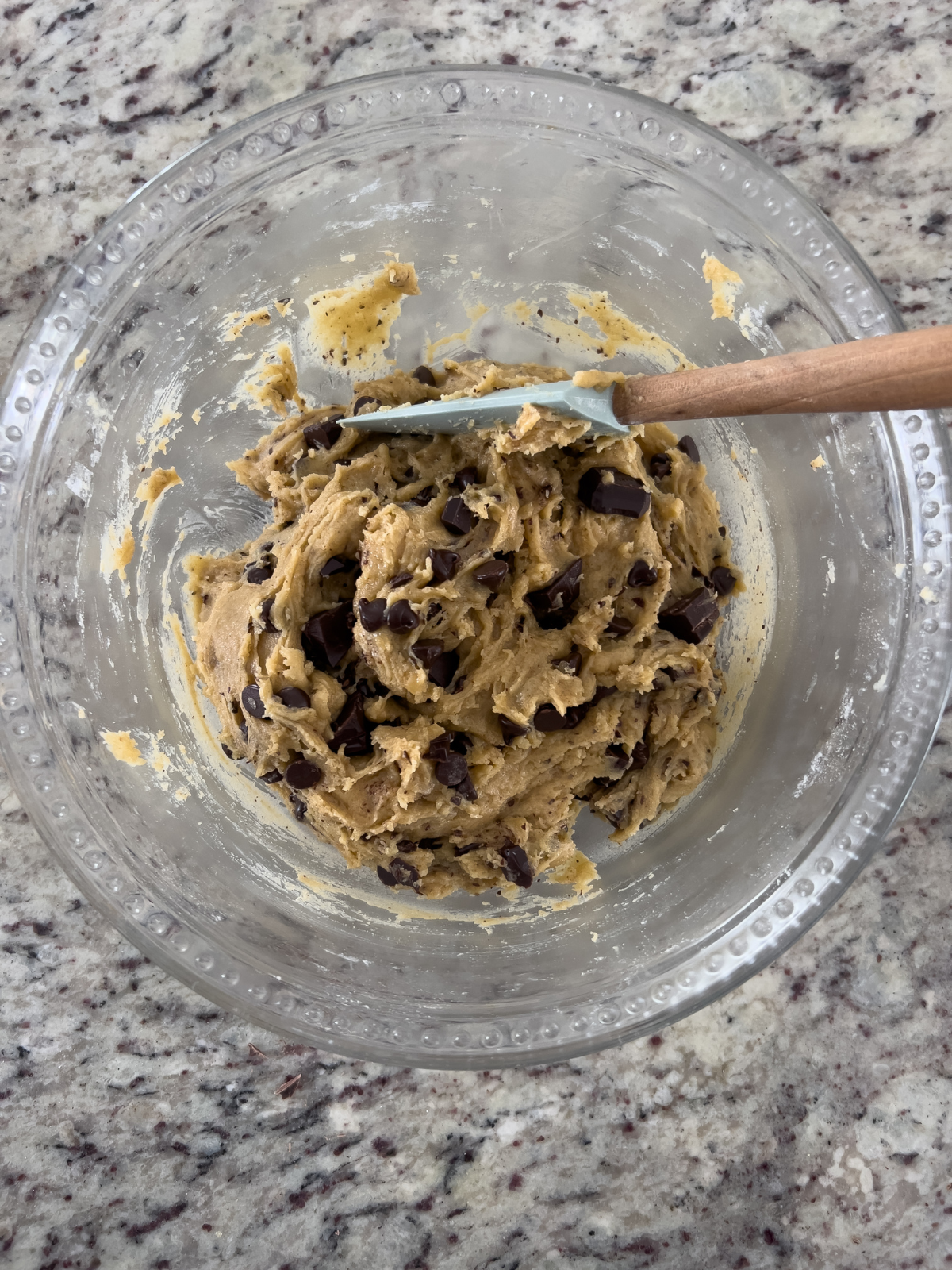 The browned butter sourdough discard chocolate chip cookie dough sits in a glass mixing bowl with a rubber spatula in it.