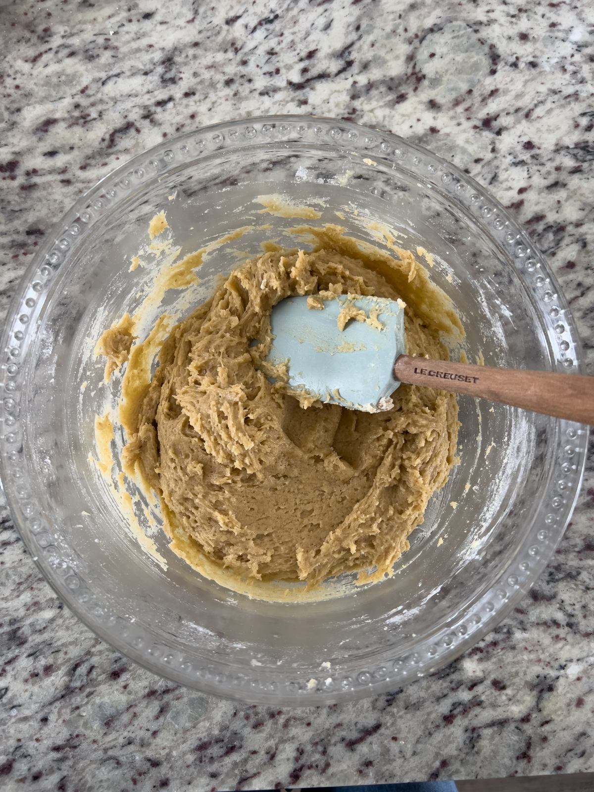 The sourdough discard cookie dough sits in a glass mixing bowl with a rubber spatula in it. Chocolate chips have not yet been added.