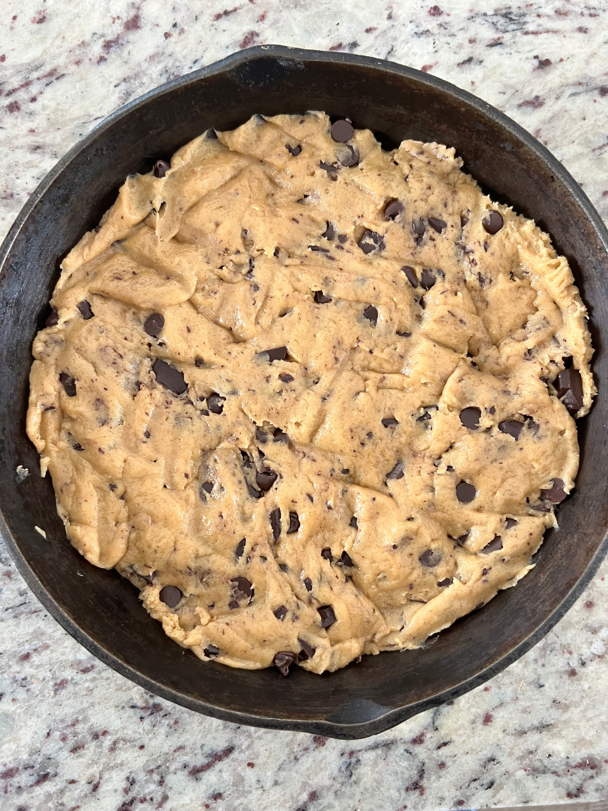 Sourdough chocolate chip cookie dough sits pressed in a cast-iron skillet preparing to bake.