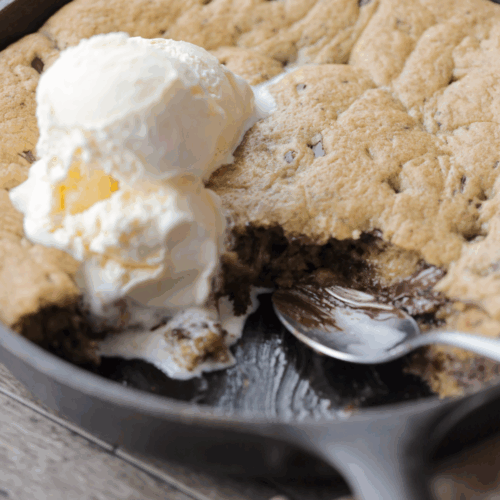 A closeup picture of the sourdough brown butter chocolate chip skillet cookie with a spoon and a couple scoops of ice cream on top.