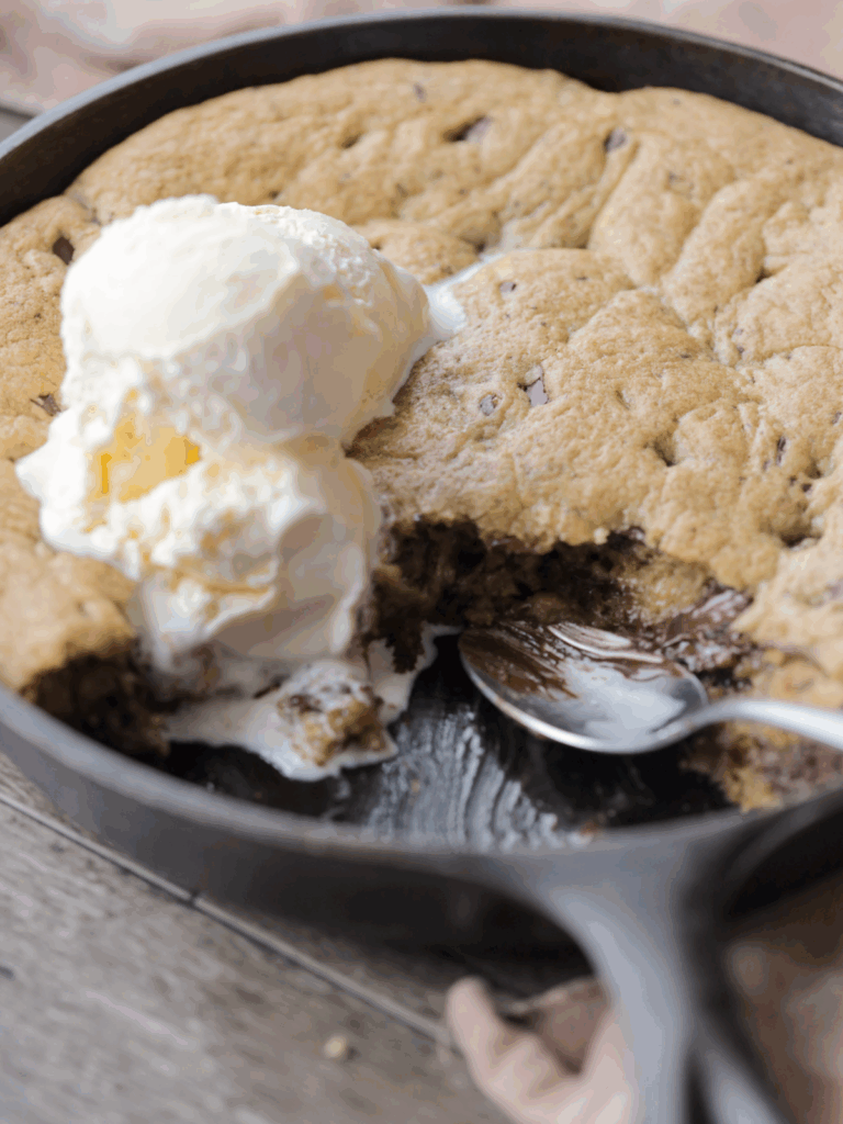A closeup picture of the sourdough brown butter chocolate chip skillet cookie with a spoon and a couple scoops of ice cream on top.