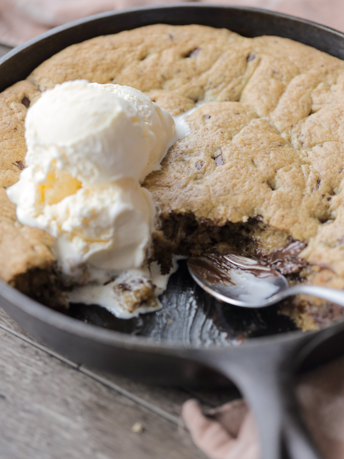 A closeup picture of the sourdough brown butter chocolate chip skillet cookie with a spoon and a couple scoops of ice cream on top.