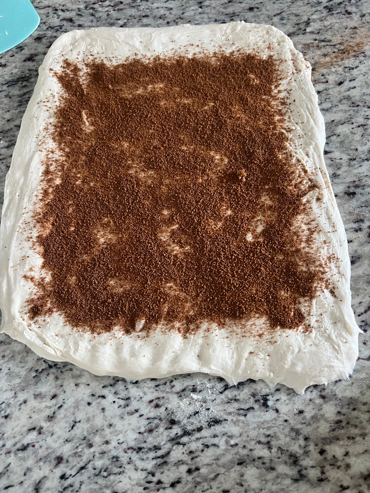 The ground cinnamon and brown sugar is shown spread over the dough leaving an inch around the edges.