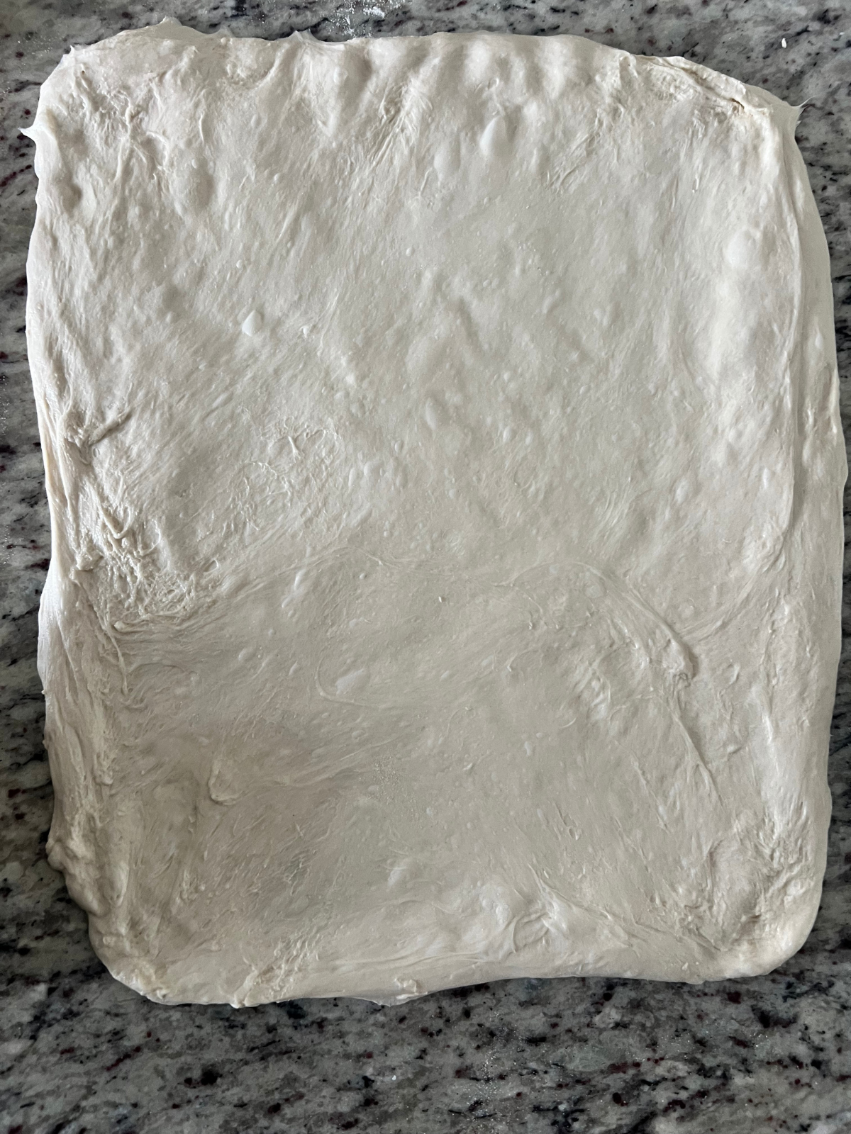 The sourdough dough has been stretched out into a rectangle to prepare to add the brown sugar and cinnamon.