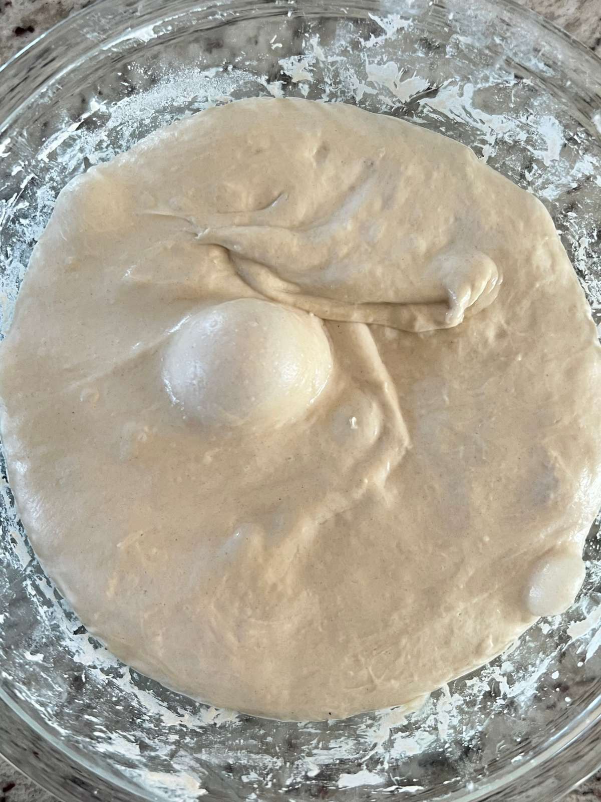 A glass mixing bowl holds sourdough dough that has been bulk fermented. 
