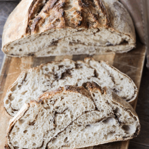 Two slices of sourdough cinnamon brown sugar bread sit on a wooden cutting board. Half of the loaf sits behind the slices.