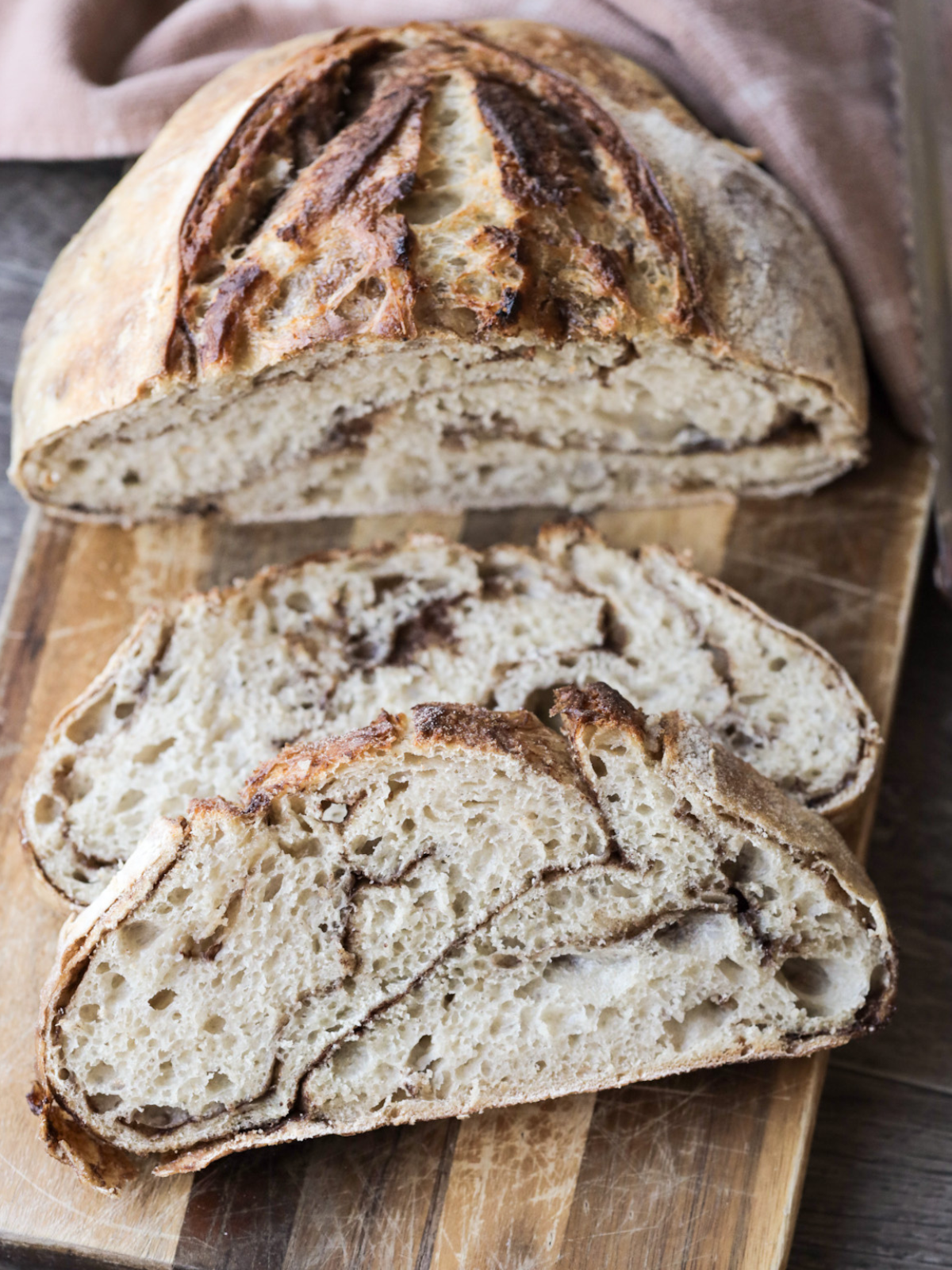Two slices of sourdough cinnamon brown sugar bread sit on a wooden cutting board. Half of the loaf sits behind the slices. 