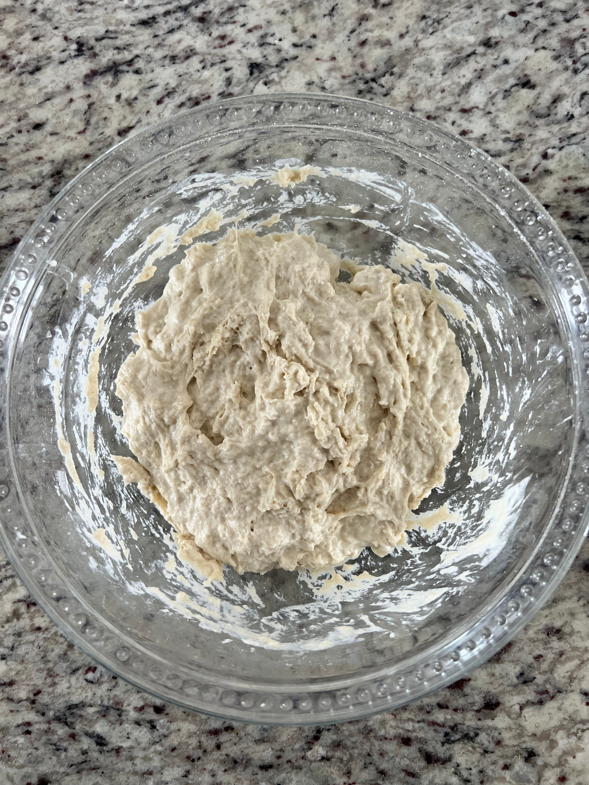 A glass mixing bowl holds a shaggy sourdough dough. 