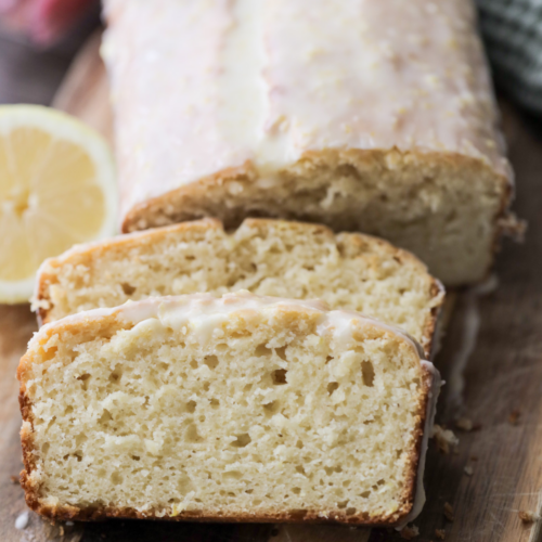 Sourdough lemon pound cake sits on a wooden cutting board behind two slices of the cake.