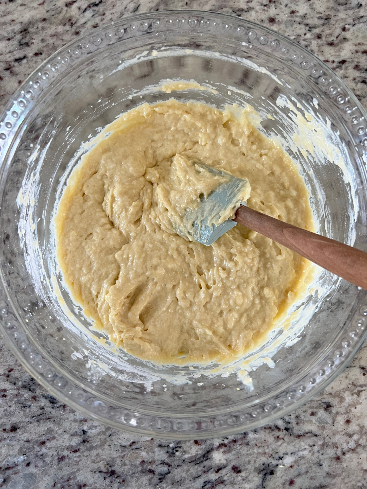 The sourdough discard lemon pound cake batter sits in a glass mixing bowl with a rubber spatula in it.