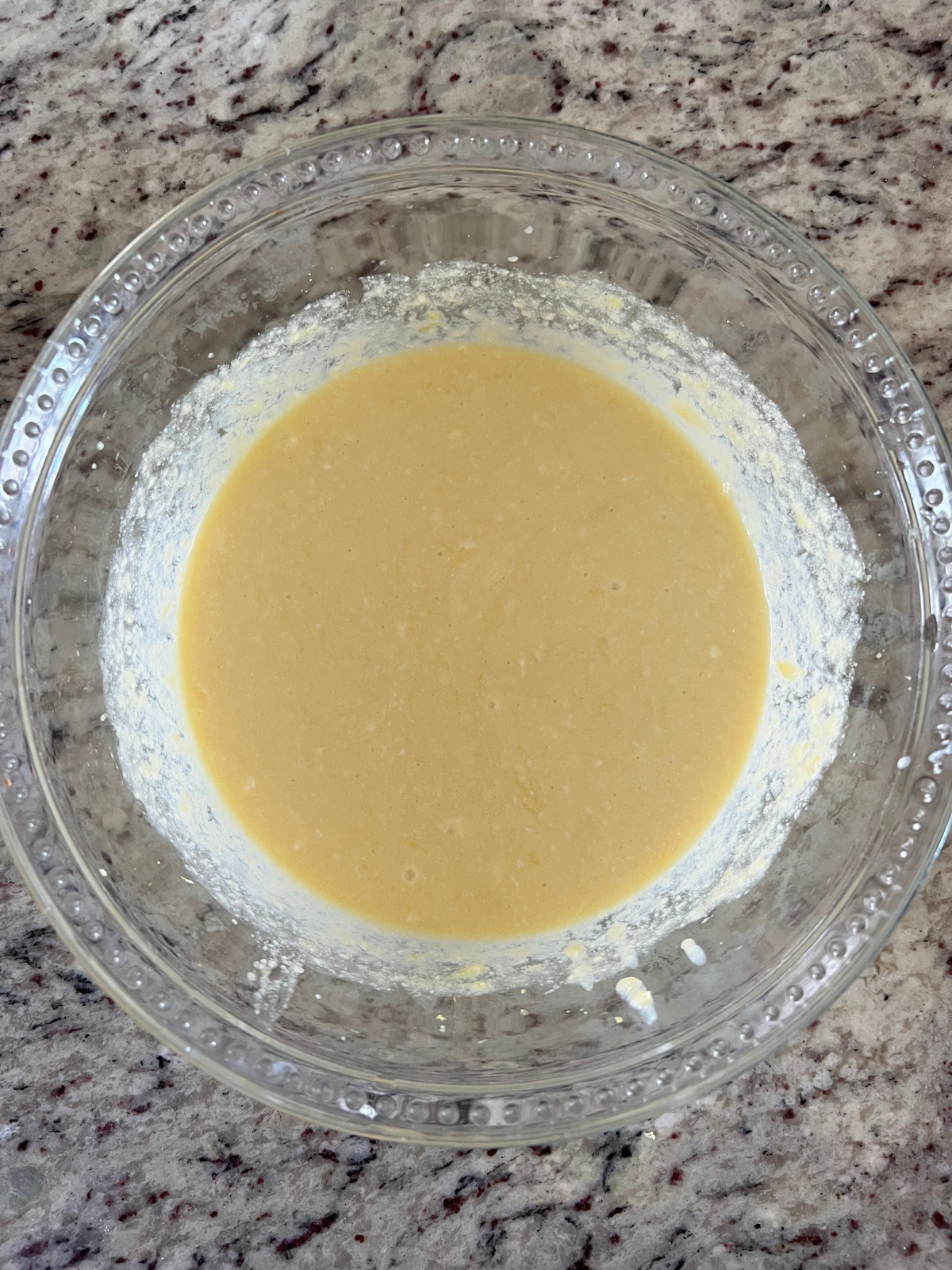 A glass mixing bowl sits with the wet ingredients needed for the sourdough lemon pound cake.