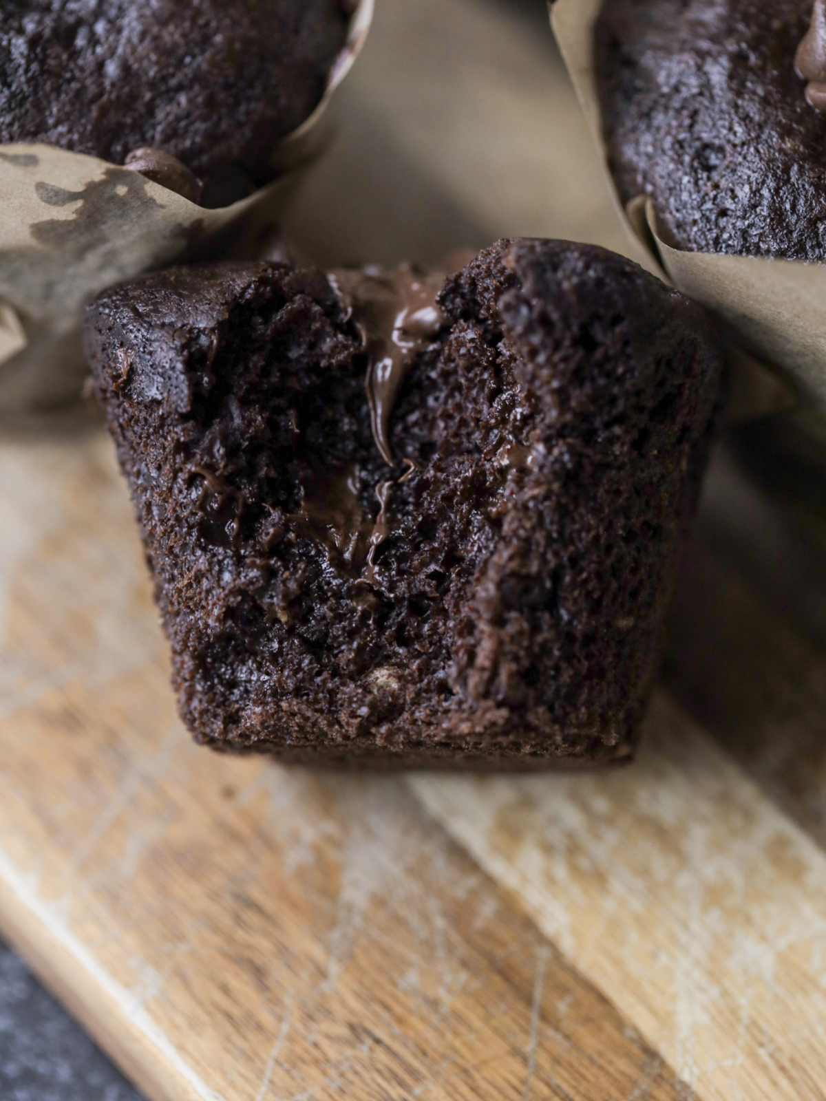 A sourdough double chocolate chip muffin sits with a bite taken out of it and melty chocolate throughout.