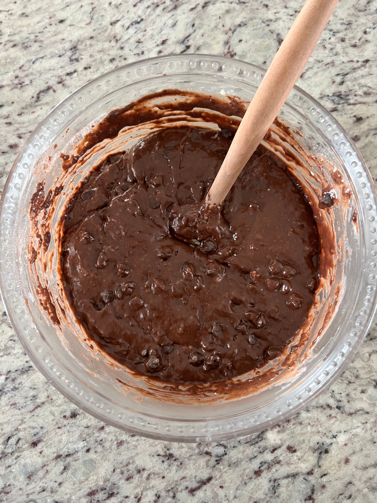 The sourdough double chocolate chip muffin batter sits in a glass mixing bowl. A rubber spatula lives in the mixing bowl.