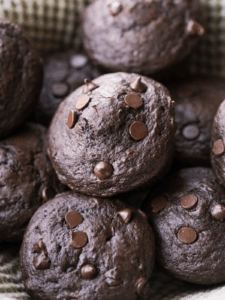 Several sourdough double chocolate chip muffins sit in a basket lined with a kitchen towel.